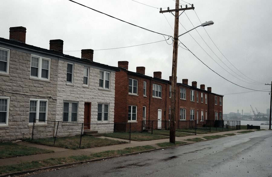WWII-era Dundalk rowhomes, some wrapped in Formstone, with the working waterfront in the grey distance